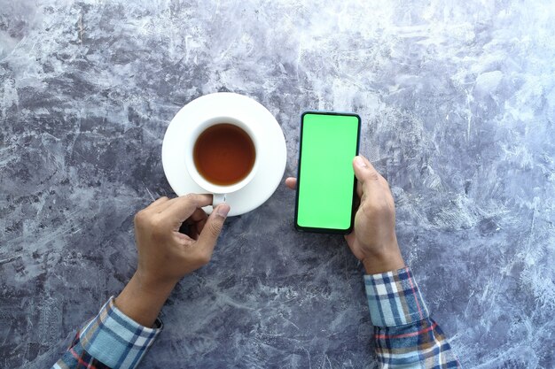 flat composition of young man hand using smart phone and drinking coffee