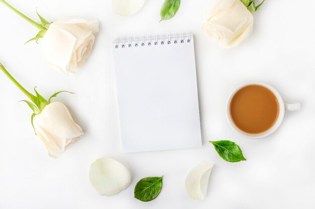 Flat lat flowers romantic composition. Morning coffee mug for breakfast, empty notebook with copy space for text or lettering and white roses.