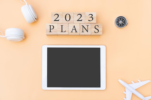 Flat lay of 2023 Plans letter on wooden cube with plane headphone compass and tablet on beige background New year planning and traveling concept Copy space top view