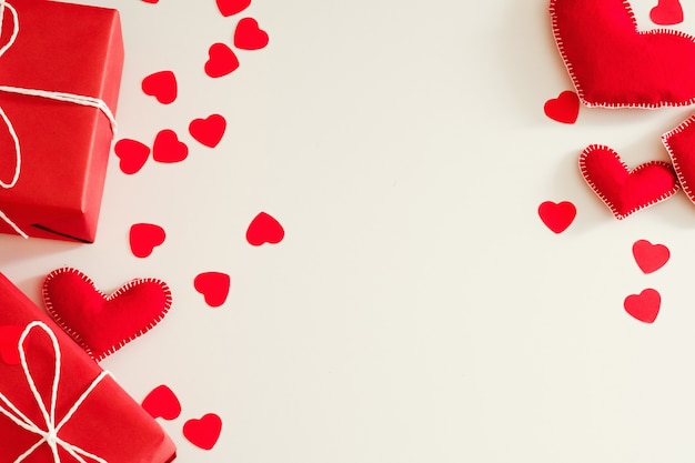 Flat lay arrangement of red handmade felt hearts and gift boxes on white