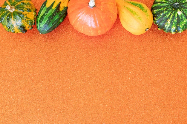 Flat lay autumn composition with copy space of decorative pumpkins on a orange glitter background