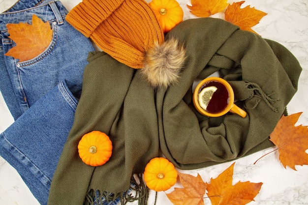 Фото Плоская осенняя композиция с осенними листьями, тыквами, чашкой горячего чая, теплым шерстяным шарфом и шапкой