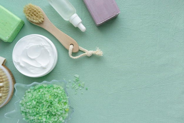 Flat lay of bath products. Massage brush, sea salt, soap and body cream on blue background, space for text.