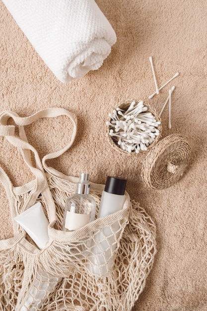 Flat lay beauty, spa, treatment, wellness composition with towel, cosmetic bottles, string bag, ear sticks on beige towel
