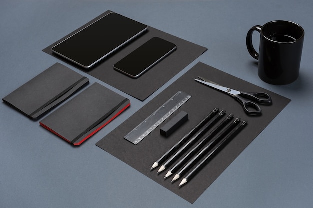 Flat lay of blank black paper sheet black stationery items and coffee cup on gray desktop mock up