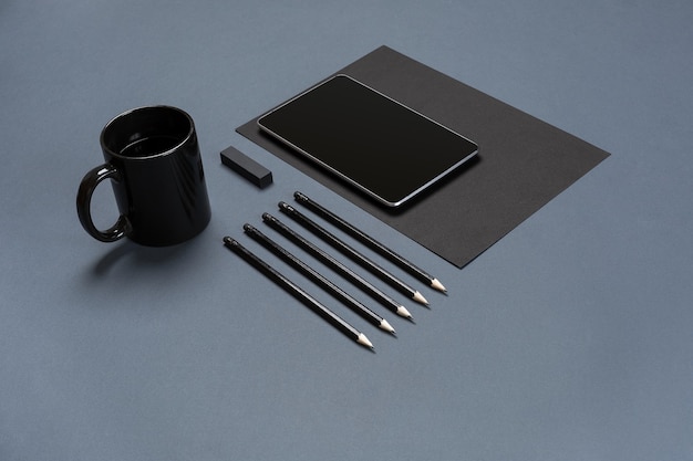 Photo flat lay of blank black paper sheet black stationery items and coffee cup on gray desktop mock up