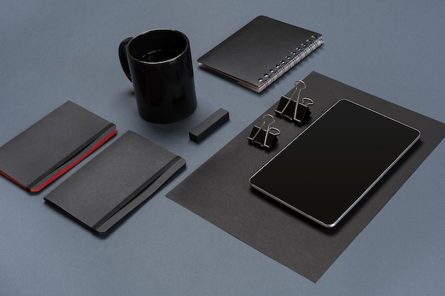 Flat lay of blank black paper sheet black stationery items and coffee cup on gray desktop mock up