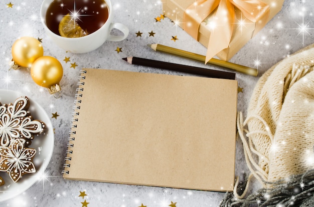 Flat lay of blank brown notebook with gift box, tea, cookies and plaid.