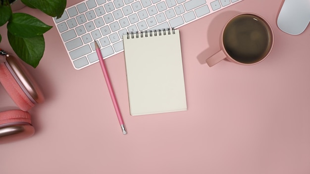 Flat lay blank notebook wireless headphone and coffee cup on pink background Feminine workplace