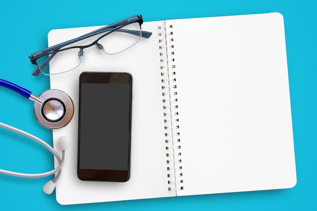 Flat lay of blue stethoscope glasses and mobile smart phone on navy blue background