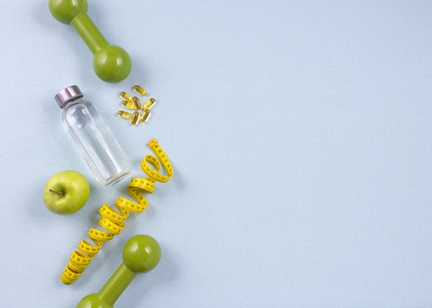 Flat lay bottle of water, measuring tape and fresh green apple on the blue background. Weight loss concept. 