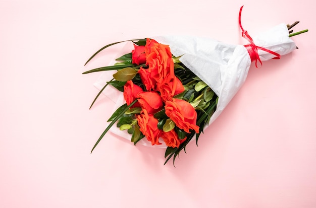 Flat lay. Bouquet of red roses and green leaves on a pink background.