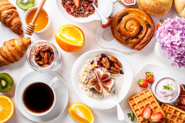 Flat lay of breakfast table with oatmeal, waffles, croissants and fruits, 