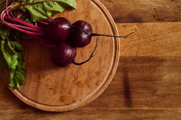 Flat lay of a bunch of fresh burgundy beetroot with green tops and leaves on a wooden cutting board . Food background of seasonal raw vegetables