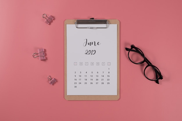 Calendario piatto laici con appunti e occhiali su sfondo rosa. giugno 2019. vista dall'alto.