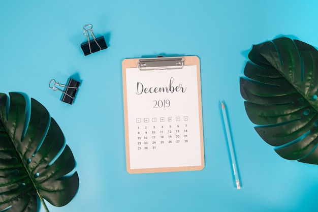 Плоский лежал календарь с буфером обмена, пальмовых листьев и карандаш на синем фоне