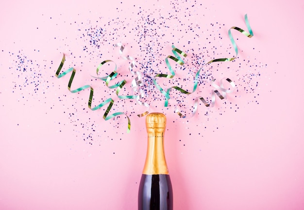 Flat lay of Celebration. Champagne bottle with colorful party streamers on pink 