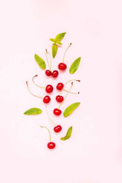 Flat lay of cherries and leaves on a pink surface.Top view