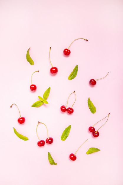 flat lay of cherries and leaves on a pink surface
