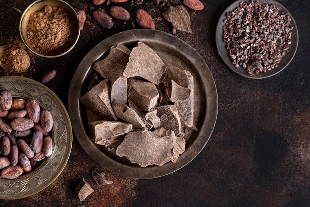 Flat lay of chocolate chunks on plate with cocoa beans and powder