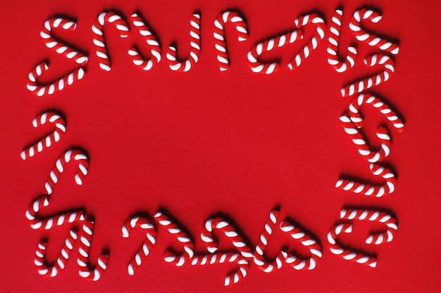 Flat lay Christmas composition with frame of candy canes on a red background Copy space for text