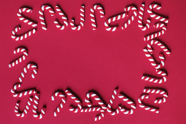 Flat lay Christmas composition with frame of candy canes on a red background Copy space for text