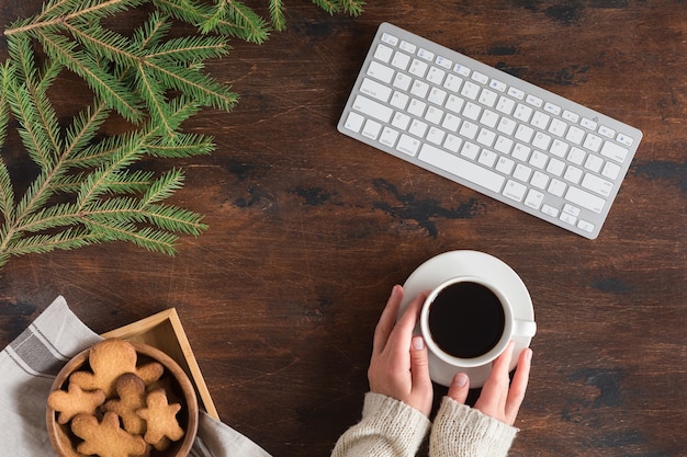 Flat lay of Christmas fir tree branch, gingerbread man, coffee cup and computer or laptop keyboard on wooden background. Top view winter, xmas and New year backdrop with space for text