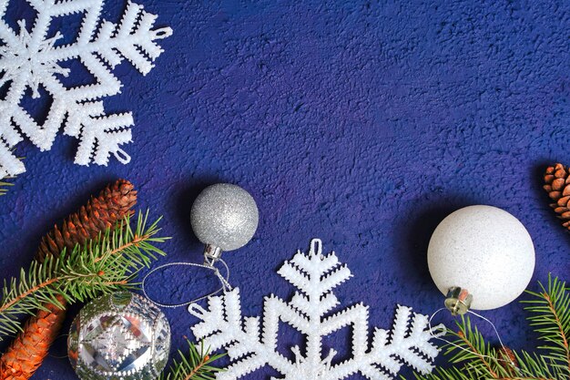 モミの枝と円錐形のフラットレイクリスマスと新年のフレームは、青いbに白いボールを雪片にします...