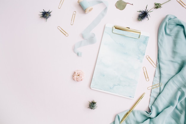 Flat lay of clipboard, rose buds, eucalyptus on pale pink