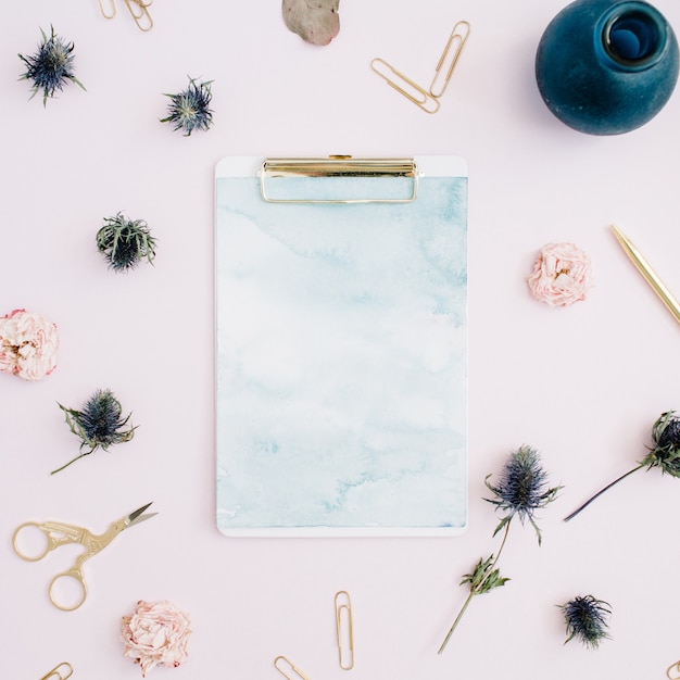 Flat lay of clipboard, rose buds, eucalyptus on pale pink