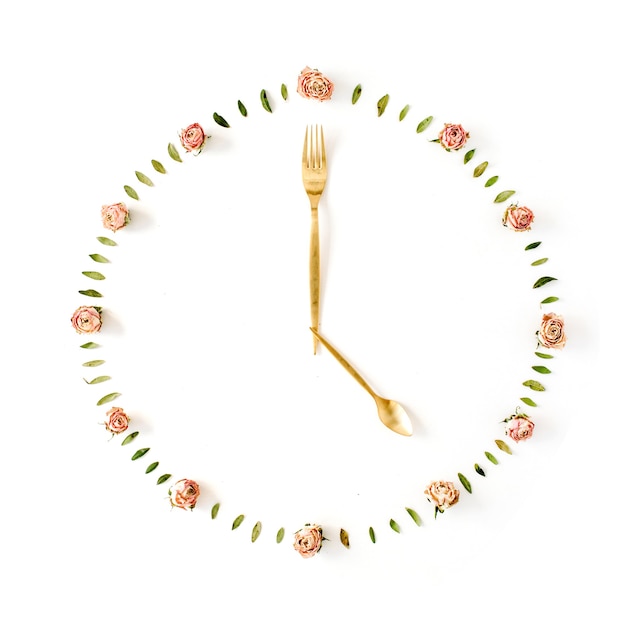 Flat lay clock face made of rose buds, spoon and fork