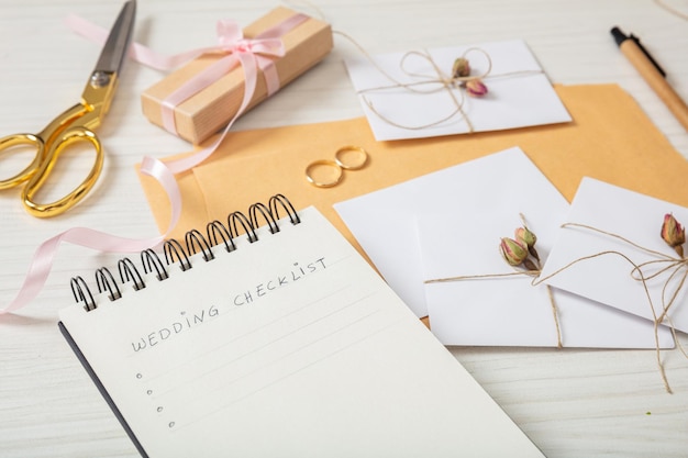 Flat lay and close up view of checklist and wedding invitations on a white wooden tabletop blank space