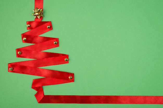 Above flat lay close up view photo of red christmas tree made of red color ribbon isolated green color background with copy space