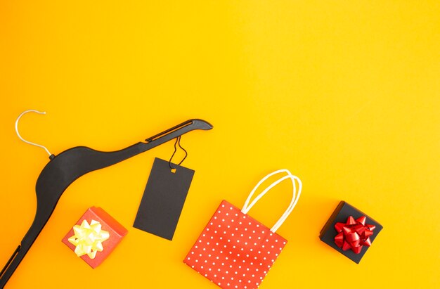 Flat lay clothes hanger with label and gift bags on a yellow background