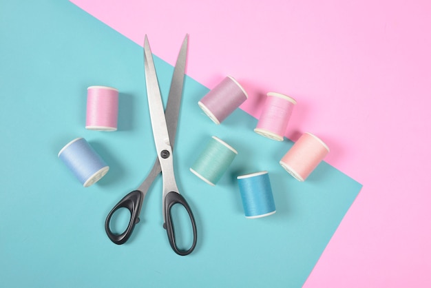 Flat lay of colored thread rolls and Scissors for sewing on two tone background.