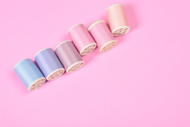 Flat lay of colored thread rolls for sewing on pink background.