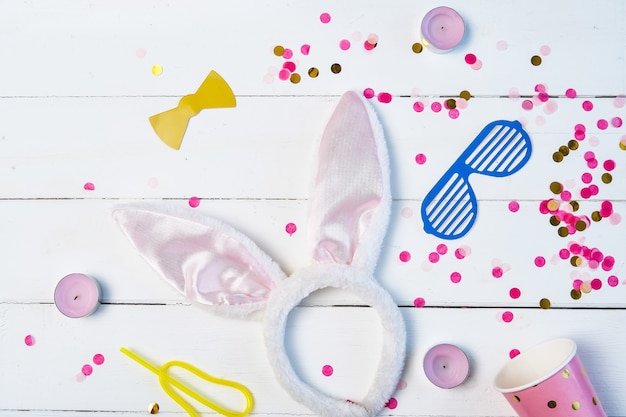 Flat lay composition of birthday party background with confetti, glass, masks, hare ears