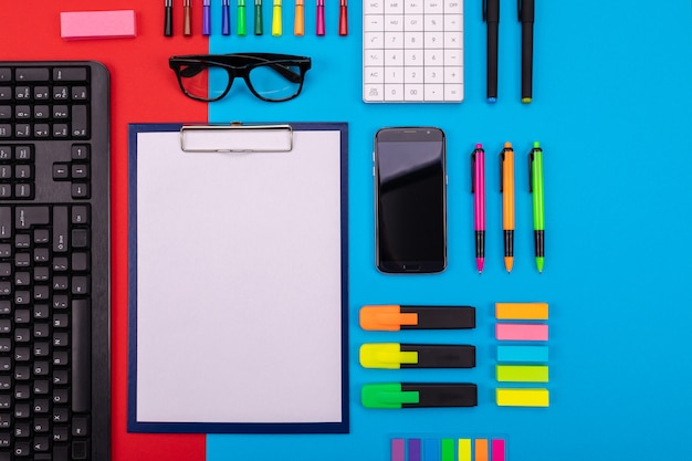 Photo flat lay composition of business desk with smartphone, clipboard, stickers, and pen on colorful blue and red