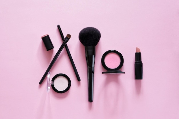 Photo flat lay composition of decorative cosmetics different makeup brushes pink background