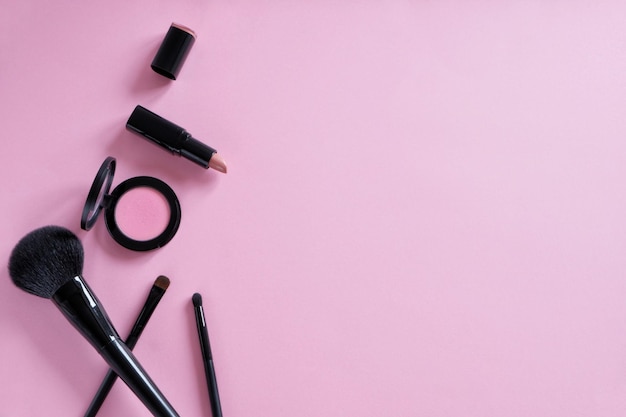 Плоская композиция из декоративной косметики, кистей для макияжа, румян, помады на розовом фоне