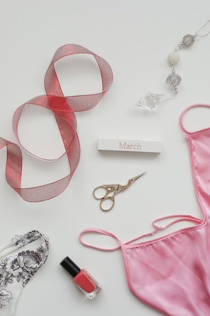 Flat lay composition of female underwear with a red ribbon and cosmetics on white background