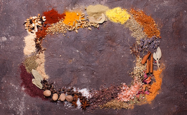 Flat lay composition frame of various spices over brown slate background, top view