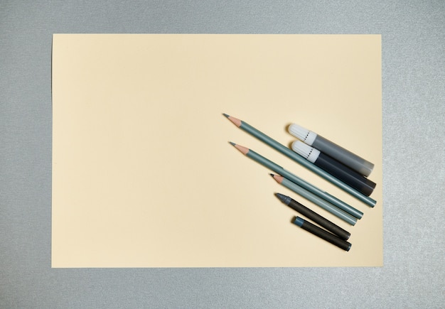 Flat lay composition of gray drawing tools on a a yellow watercolor paper. Top view on a gray background