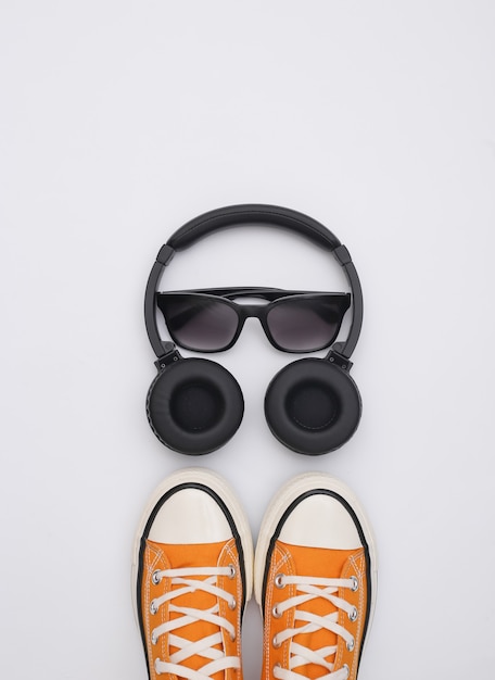 Flat lay composition of gym shoes, sunglasses and stereo
headphones on white background. youth accessories. top view