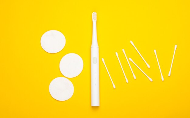 Flat lay composition of hygiene products. Toothbrush, cotton pads, ear sticks on yellow background. Top view