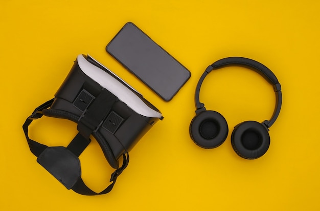 Flat lay composition of modern gadgets. vr helmet, headphones and smartphone on yellow background. top view