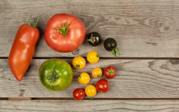 Photo flat lay composition of multicolored tomatoes different sizes on a wooden background