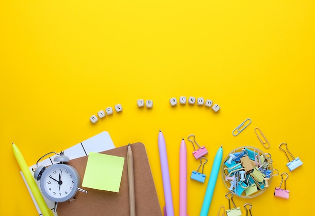 Flat lay composition of notebook, pencil, pens, binders, alarm clock. 