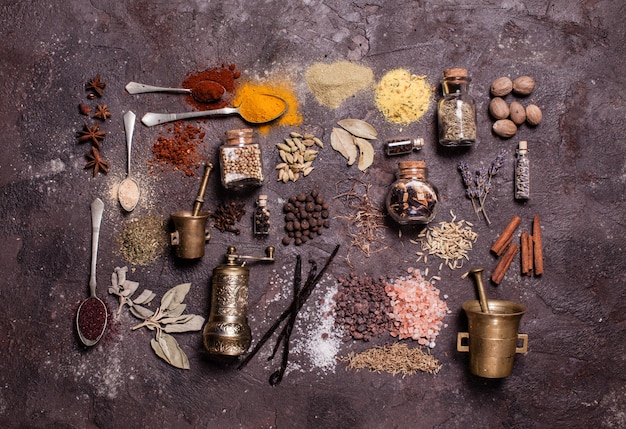 Flat lay composition of various spices and mortars over brown slate background, top view