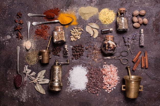 Flat lay composition of various spices and mortars over brown slate background, top view